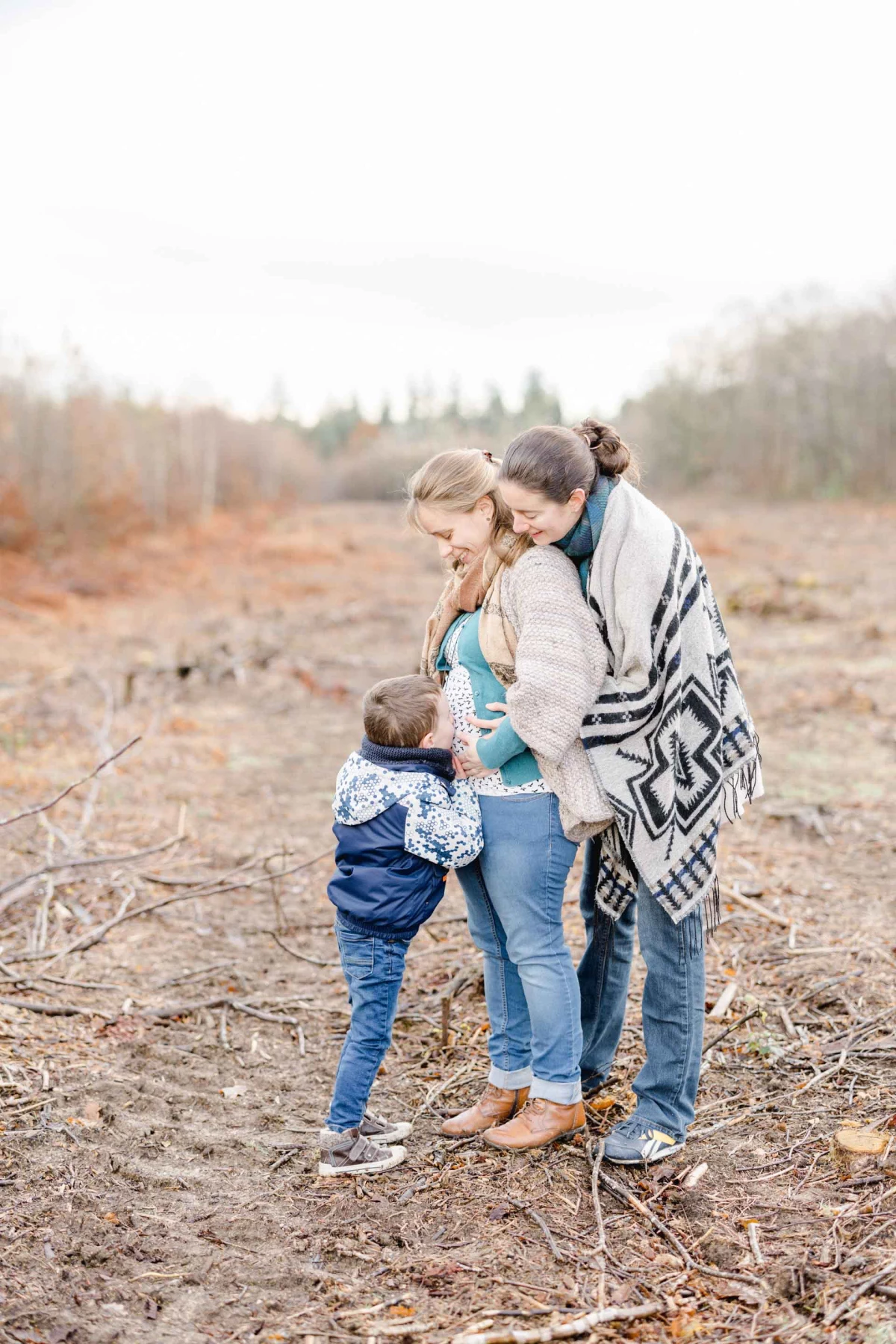 Séance famille en plein air : mère enceinte entourée de ses deux enfants dans un champ automnal, moment de tendresse et complicité dans une lumière douce
