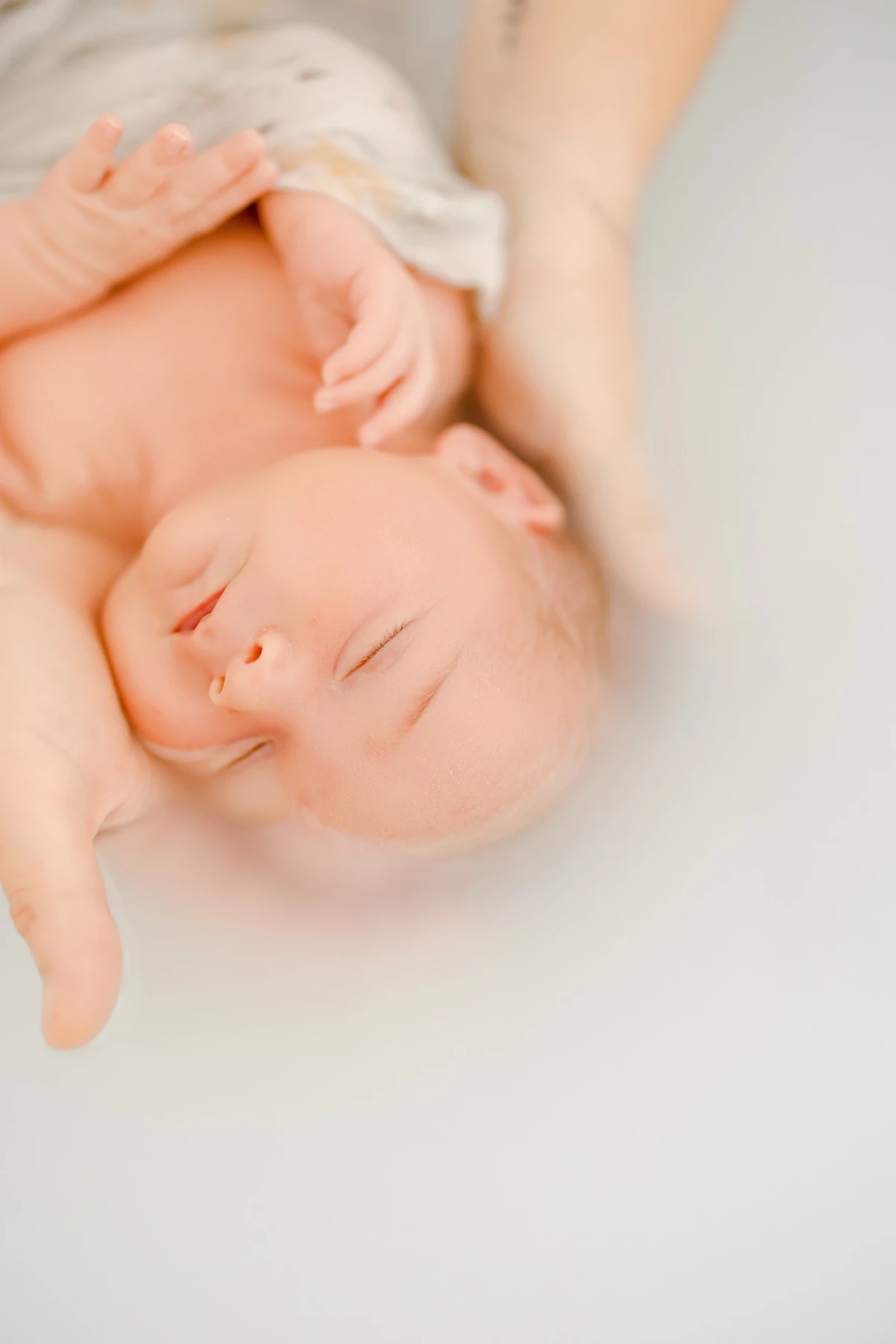 Séance bain bébé en studio : nouveau-né serein dans les mains de sa maman, ambiance douce et cocooning
