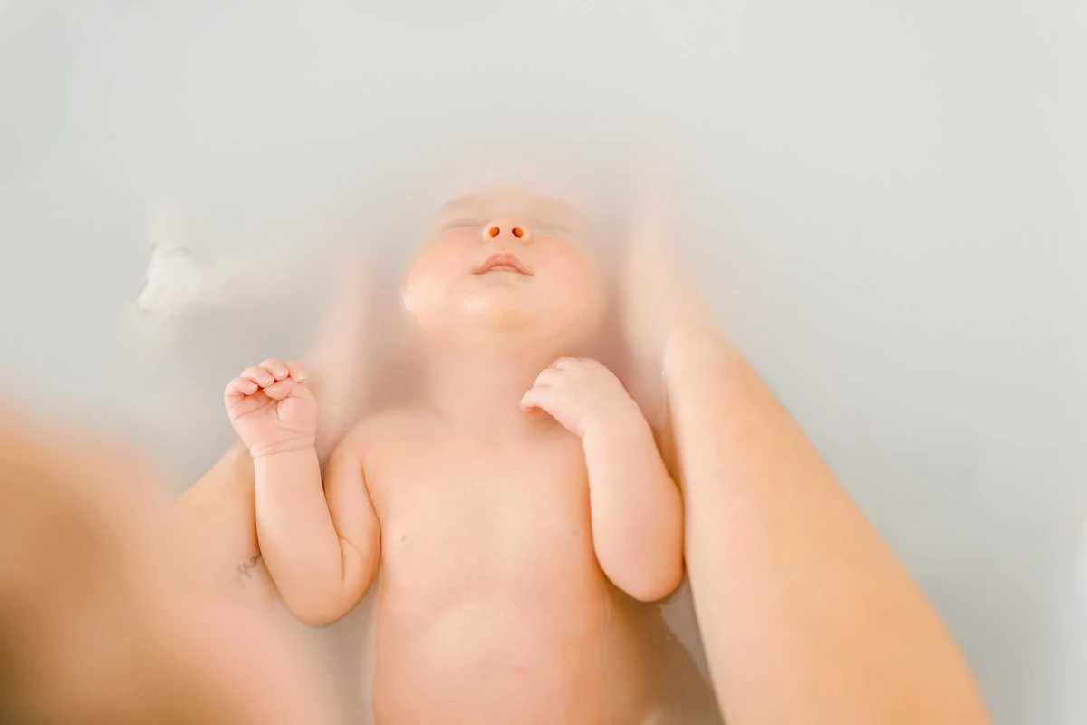 Séance bain bébé au studio : nouveau-né allongé dans l'eau laiteuse, ambiance de douceur et de sérénité absolue