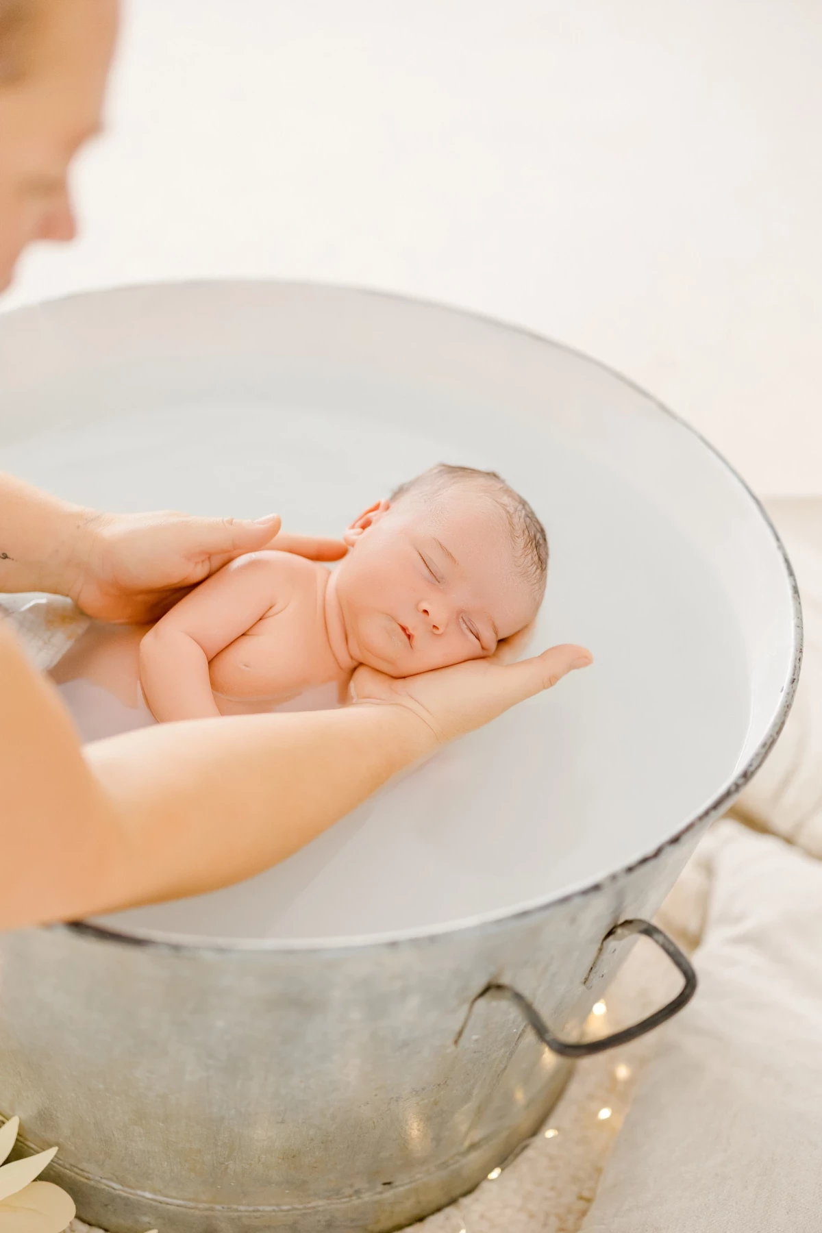 Séance nouveau-né au studio : bébé endormi dans les mains de sa maman lors d'un bain, instant de tendresse et de sérénité