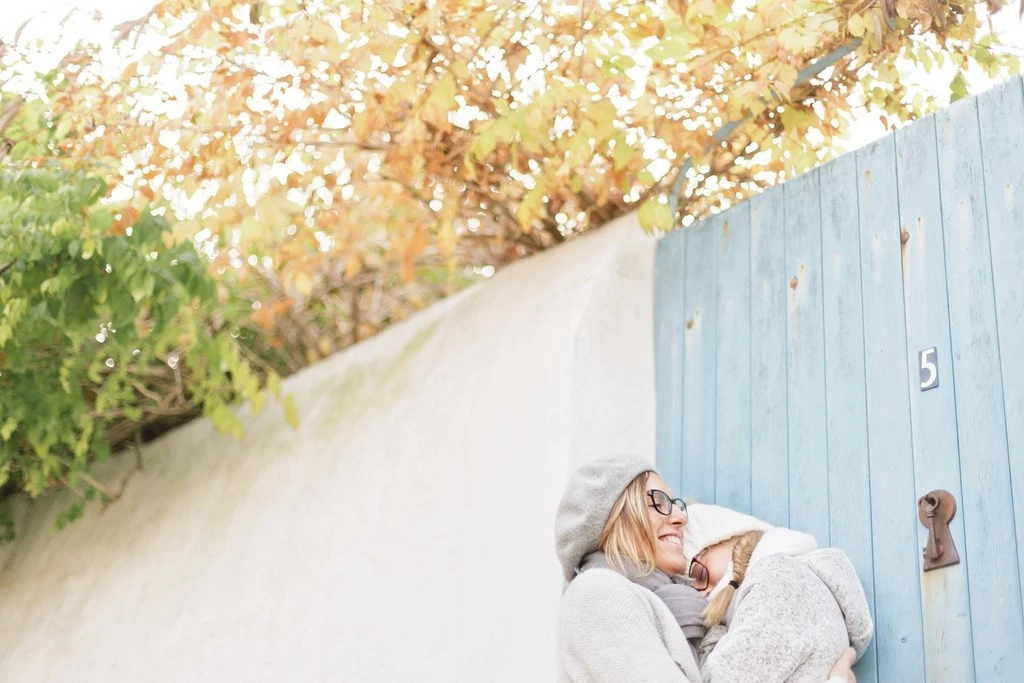 Portrait de famille tendresse : femme senior en cardigan gris tient bébé contre elle, mur bleu ciel en arrière-plan, lumière dorée automne