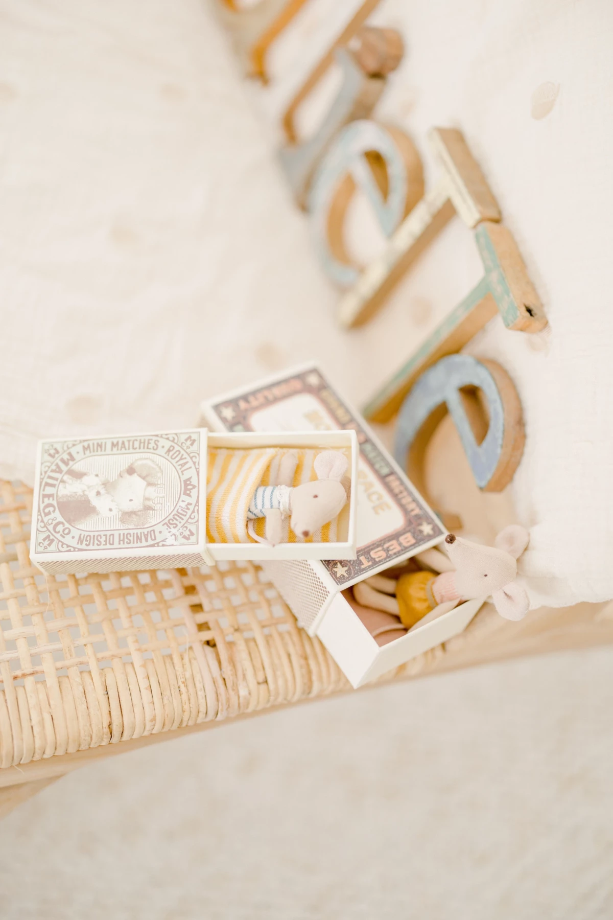 Boîte artisanale contenant petits doudous beiges, disposée sur chaise cannée, ambiance douce en studio