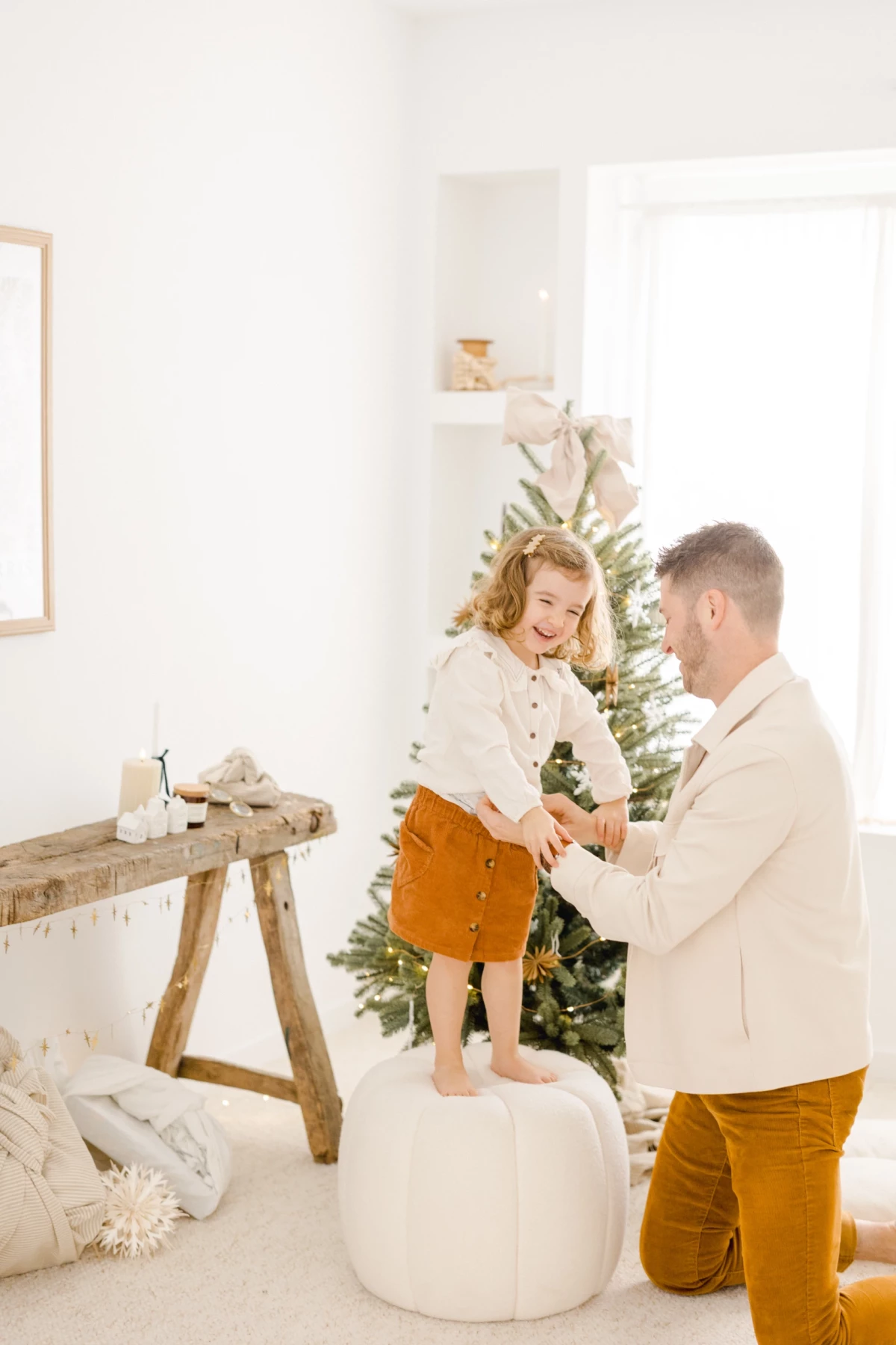 Père et enfant partageant un moment complice devant le sapin de Noël dans un intérieur blanc et lumineux