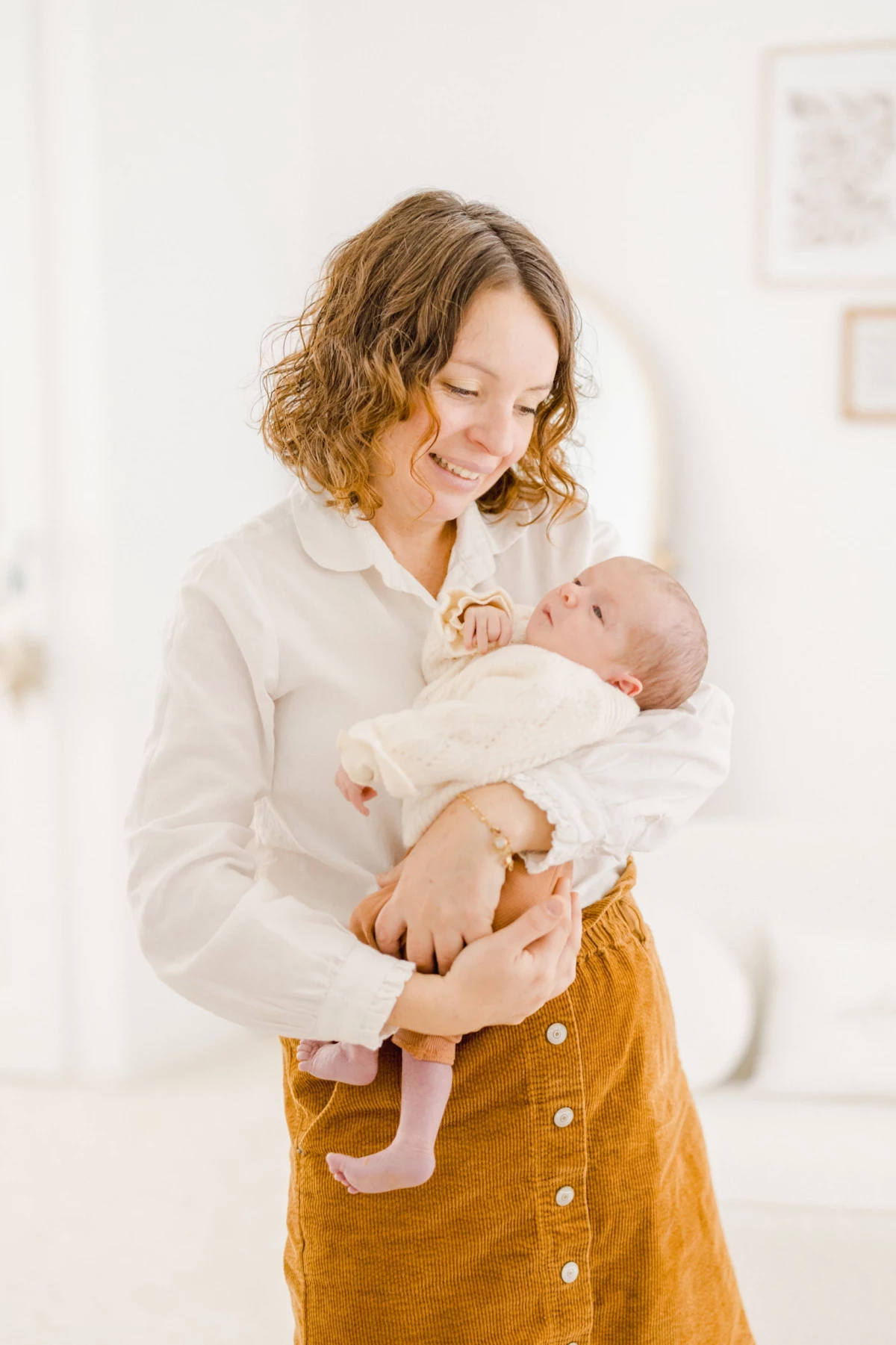 Mère tenant tendrement son nouveau-né dans ses bras, vêtue de blanc, sur fond clair et lumineux