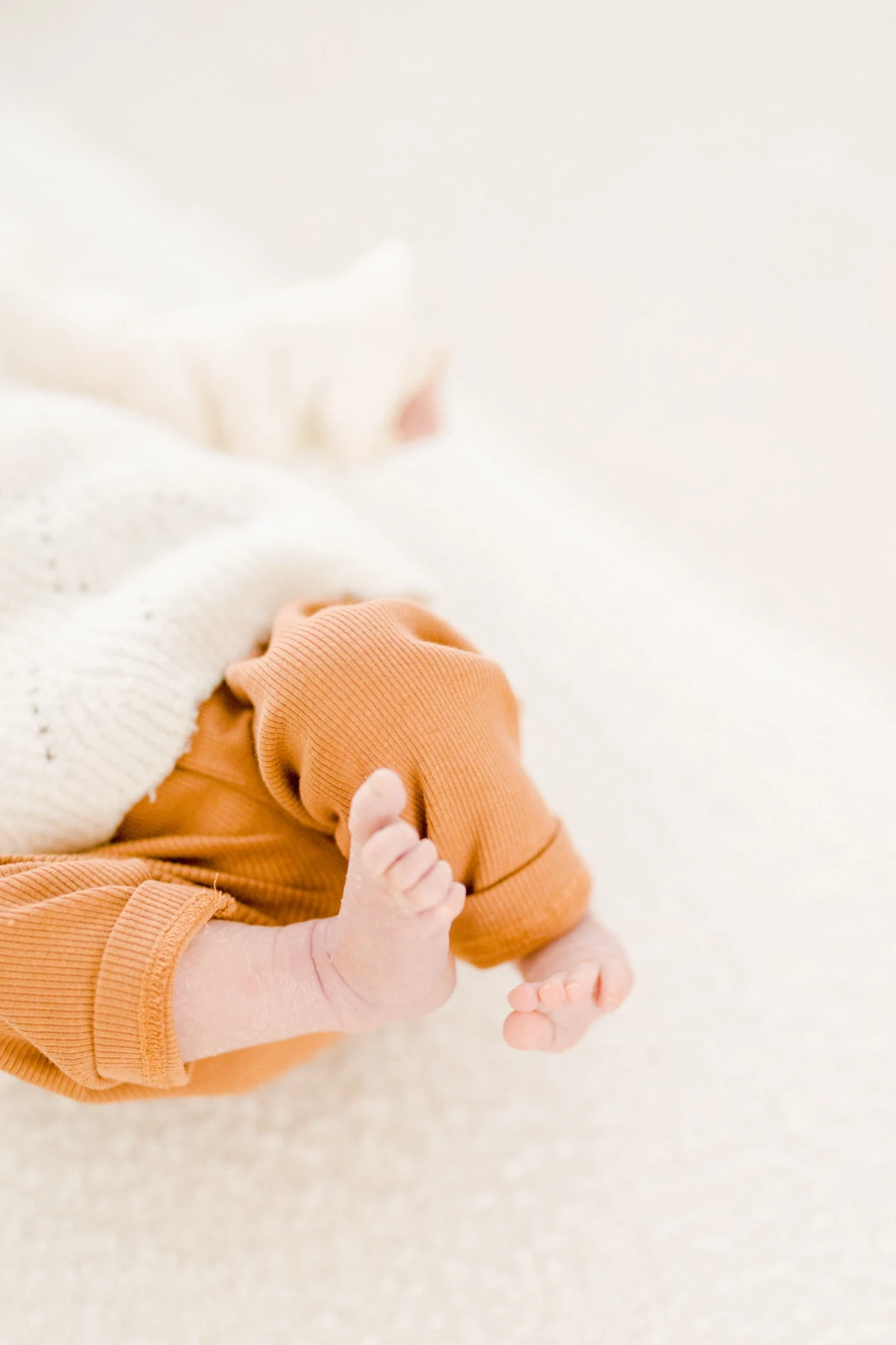 Pieds délicats d'un bébé en vêtement orange posé sur une couverture blanche immaculée