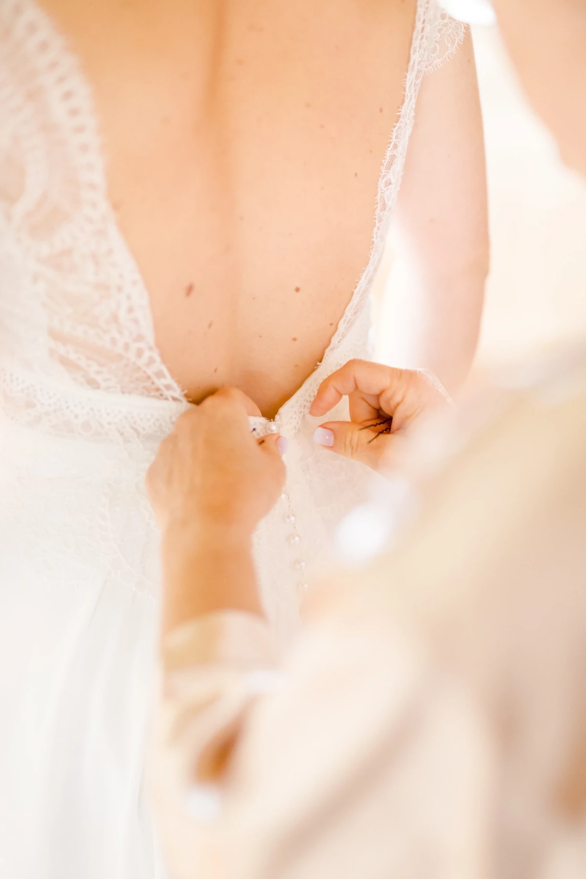 Mains de la mariée attachant délicatement les boutons de sa robe de mariée en dentelle blanche