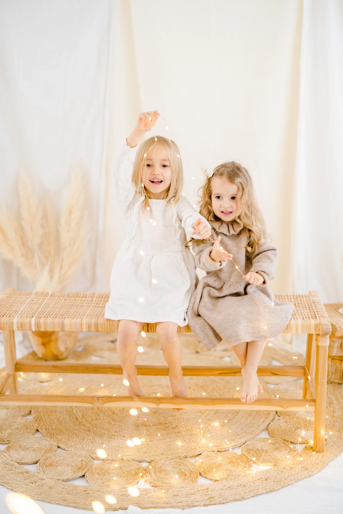 Séance famille en studio : deux jeunes sœurs jouent joyeusement sur un banc doré, atmosphère lumineuse et naturelle en Vendée