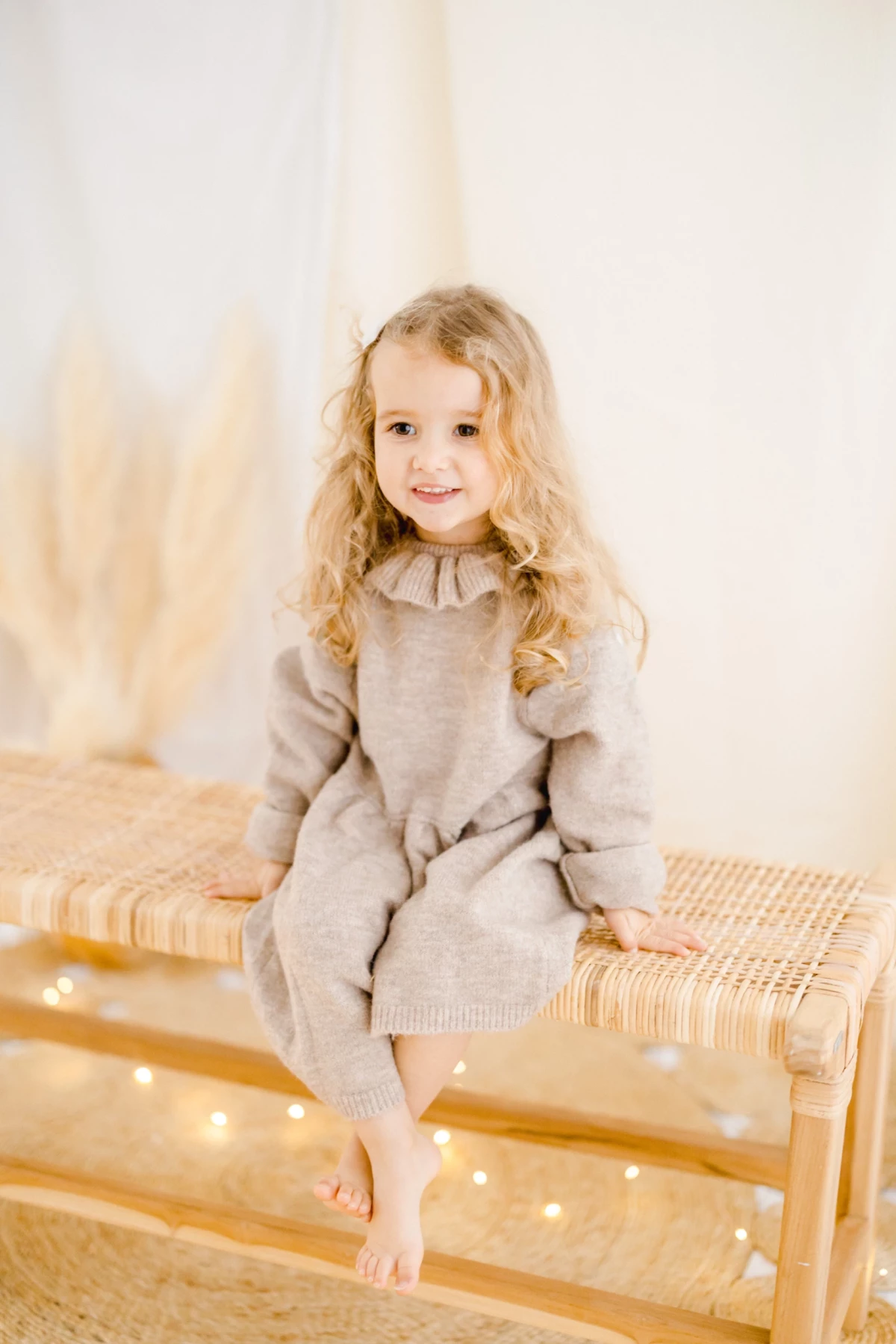 Séance portrait enfant en studio : fillette souriante assise sur un banc en rotin dans une ambiance douce et lumineuse