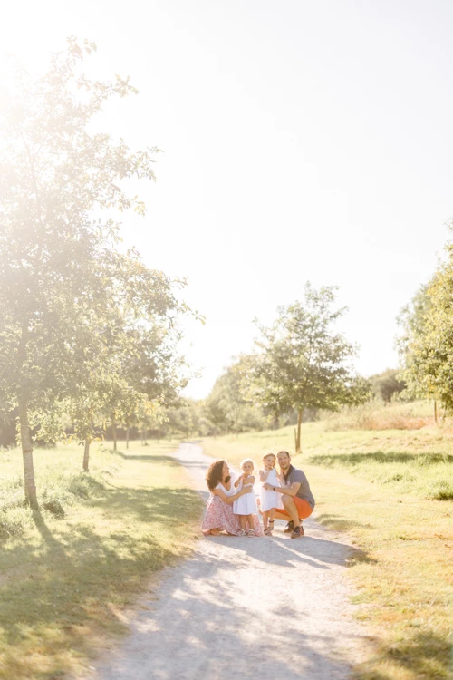 Séance famille en plein air : parents et enfants assis sur un chemin de campagne bordé d'arbres, lumière dorée, ambiance tendre et complice