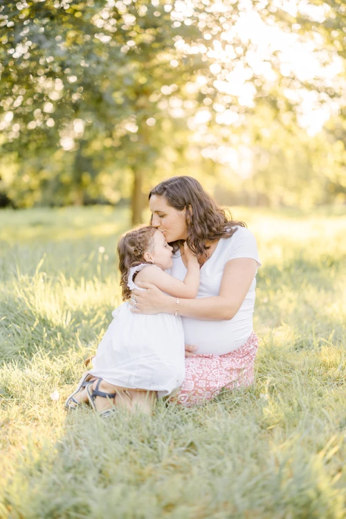 Séance photo famille en extérieur : mère et fille s'embrassant tendrement dans un champ verdoyant baigné de lumière dorée
