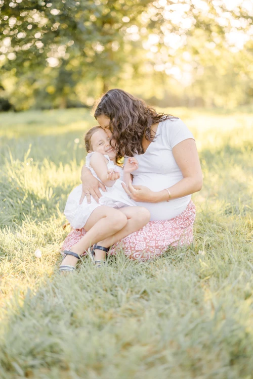 Séance photo famille en extérieur : mère et enfant en tendre complicité dans un champ verdoyant baigné de lumière dorée, moment d'intimité authentique et doux