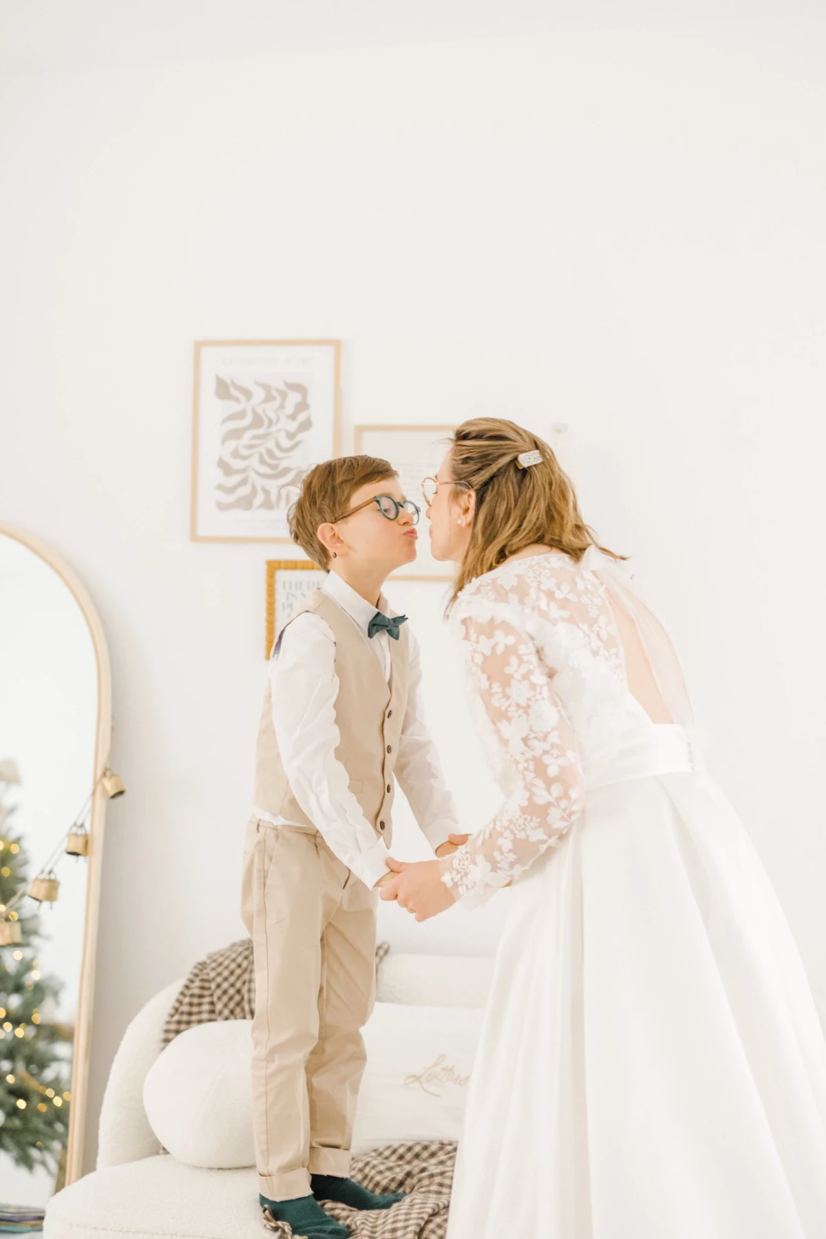 Jeune garçon en costume beige embrassant tendrement sa maman en robe de mariée blanche en dentelle