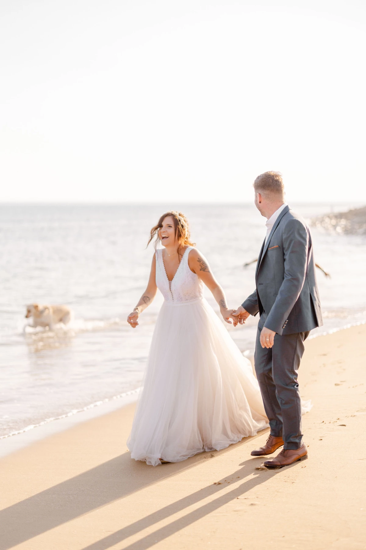 Mariage sur la plage : jeunes mariés se tenant la main dans l'eau, robe blanche élégante, lumière dorée du coucher de soleil, ambiance romantique et intemporelle en Vendée
