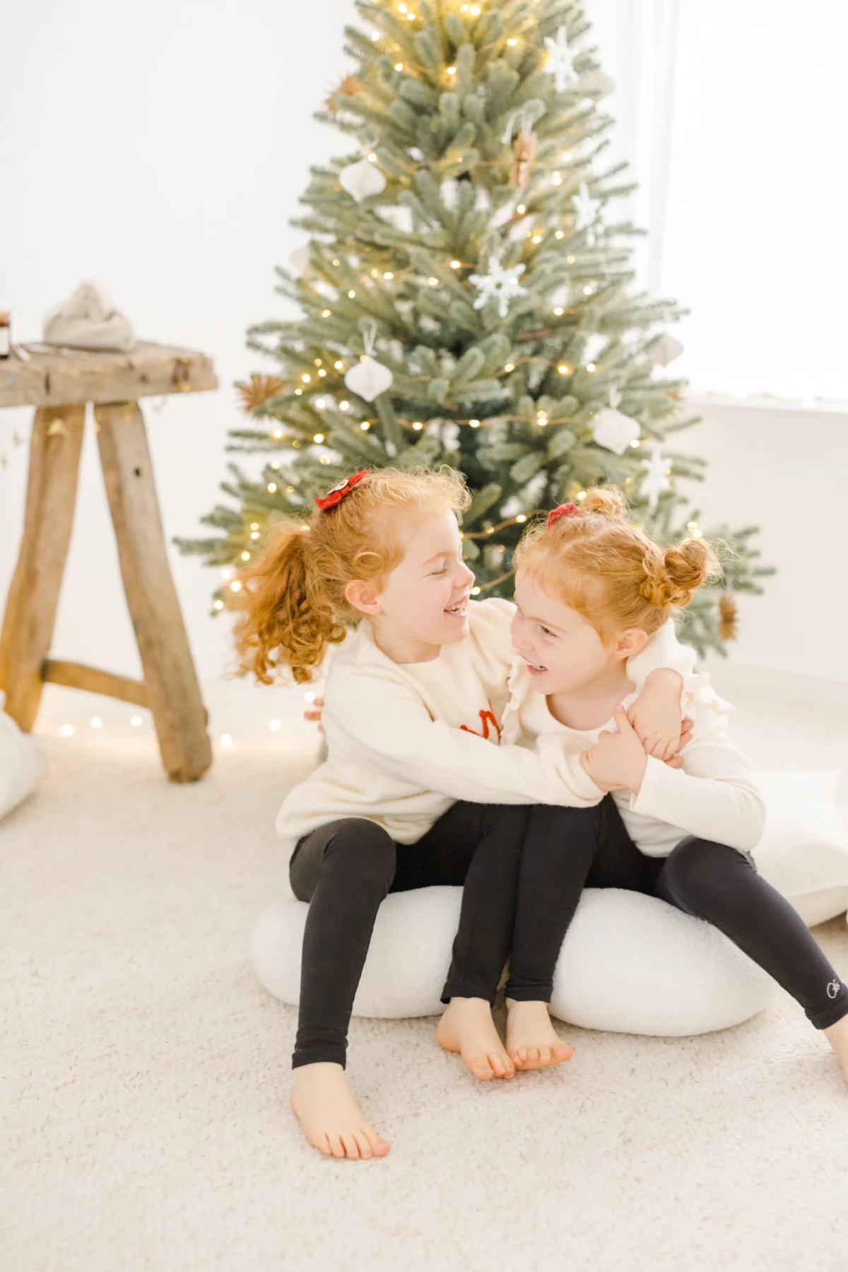 Deux petites filles complices enlacées devant un sapin de Noël enneigé dans un studio lumineux