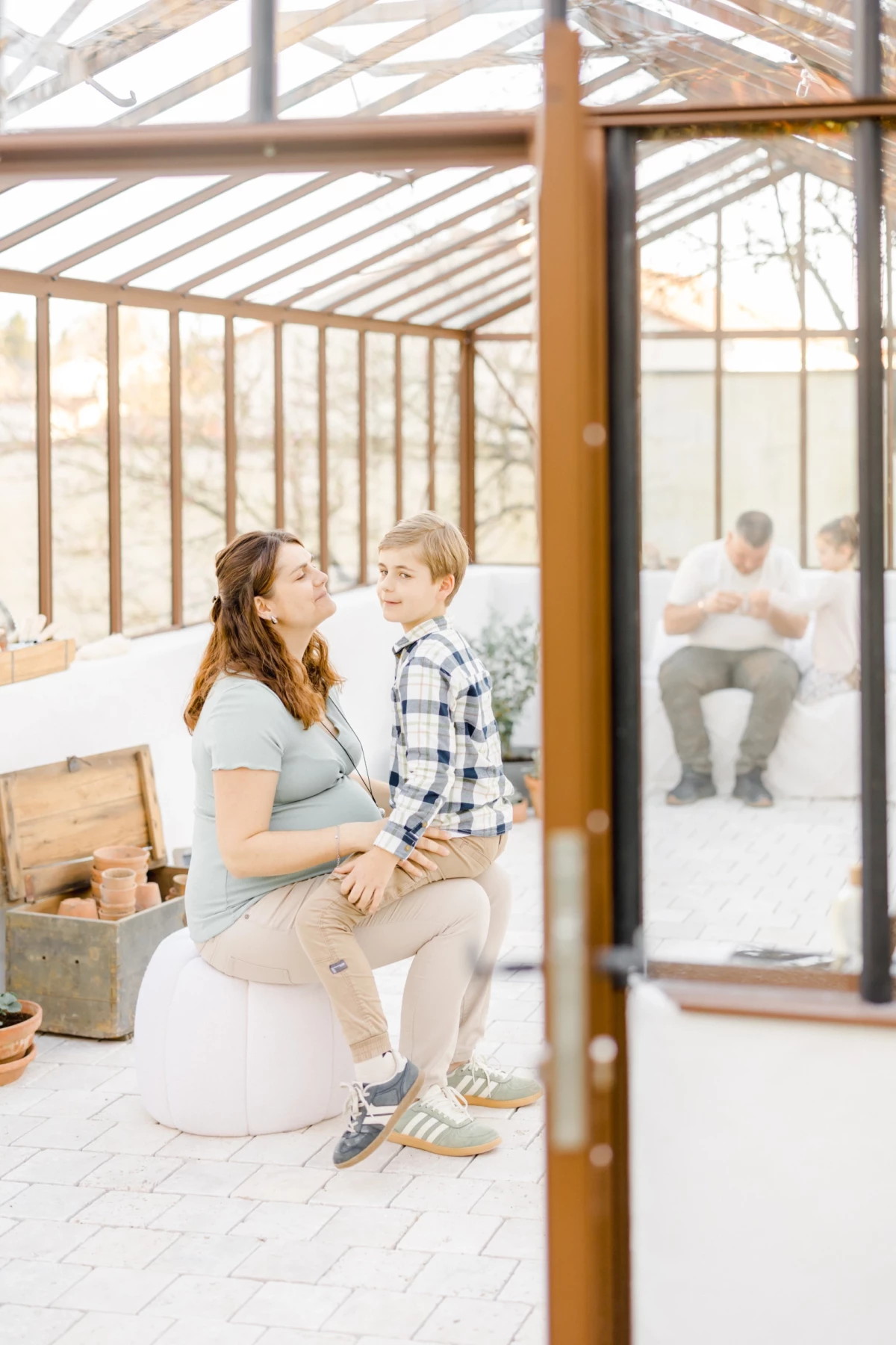Séance grossesse en famille : maman enceinte et son fils partagent un moment de tendresse dans une verrière lumineuse