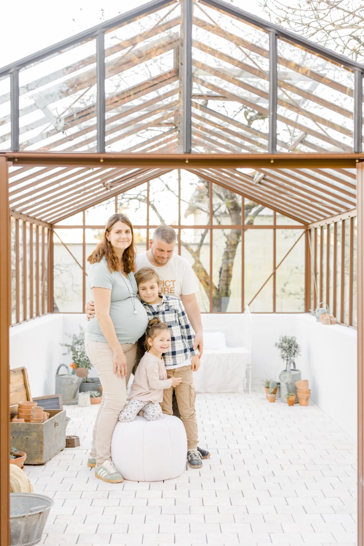 Séance grossesse en famille dans une verrière : parents et enfants réunis dans une ambiance lumineuse et naturelle pleine de douceur