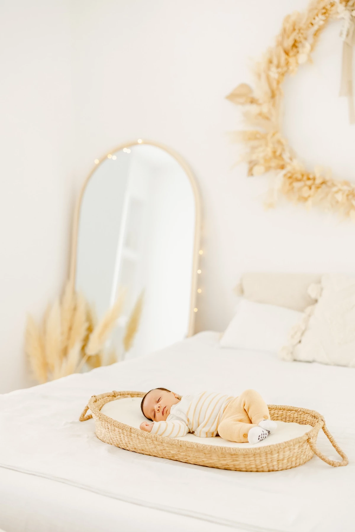 Séance nouveau-né au studio : bébé endormi paisiblement dans un couffin en osier, enveloppé de blanc, ambiance douce et épurée