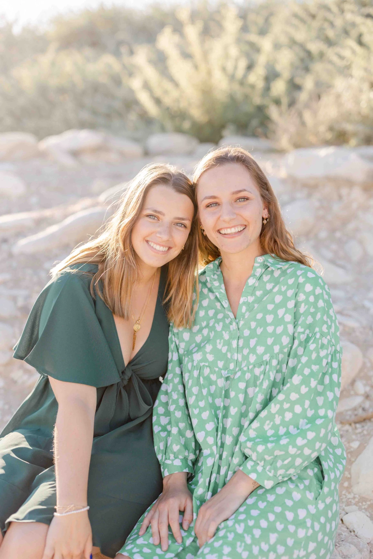Séance portrait famille : deux jeunes femmes souriantes en tenues pastel posent ensemble sur des rochers, baignées de lumière dorée, exprimant une complicité tendre et authentique