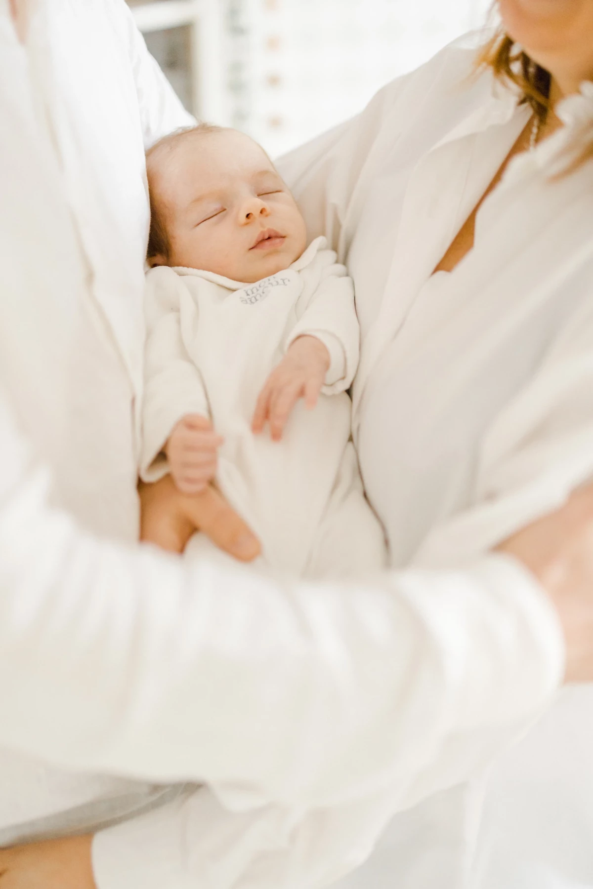 Séance nouveau-né en studio : maman berce son bébé endormi dans ses bras, drapée de voile blanc, ambiance de douceur infinie