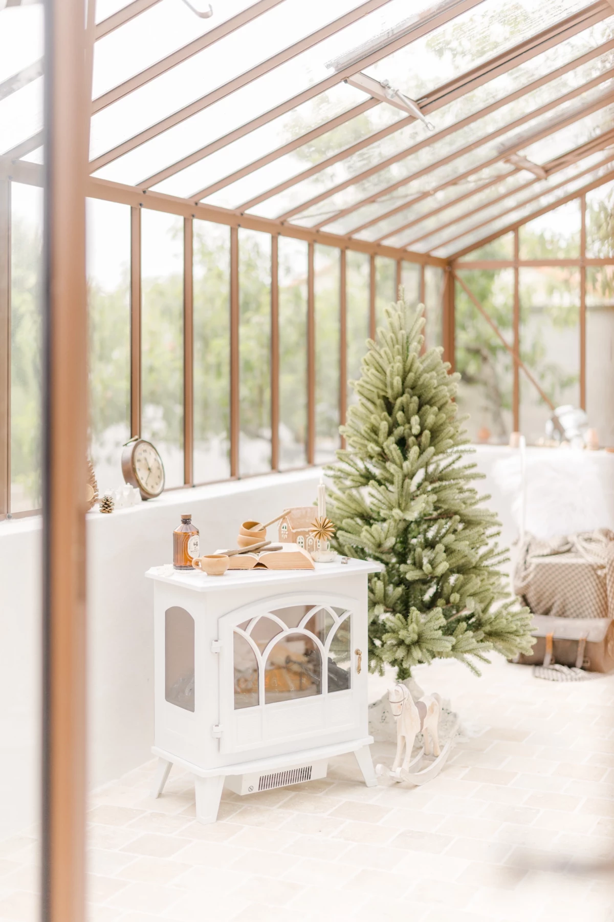 Décor séance photo Noël en studio verrière : sapin blanc et poêle vintage dans une ambiance lumineuse et épurée