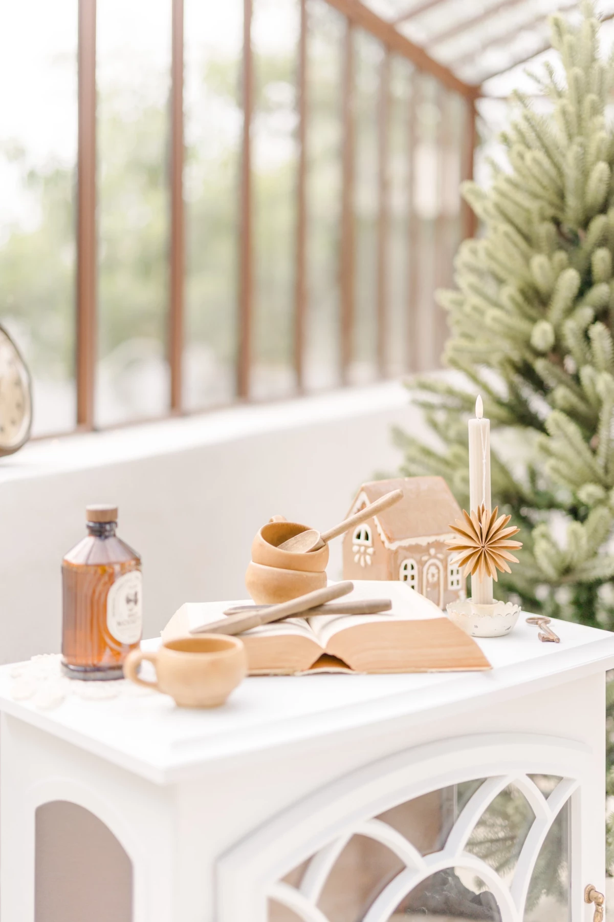Décor séance photo de Noël en studio : table blanche avec décorations naturelles beiges et sapin dans une verrière lumineuse