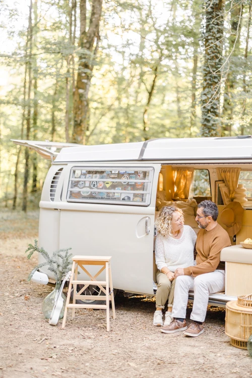 Couple senior en complicité devant camping-car vintage en forêt, moment tendre et authentique en lumière dorée