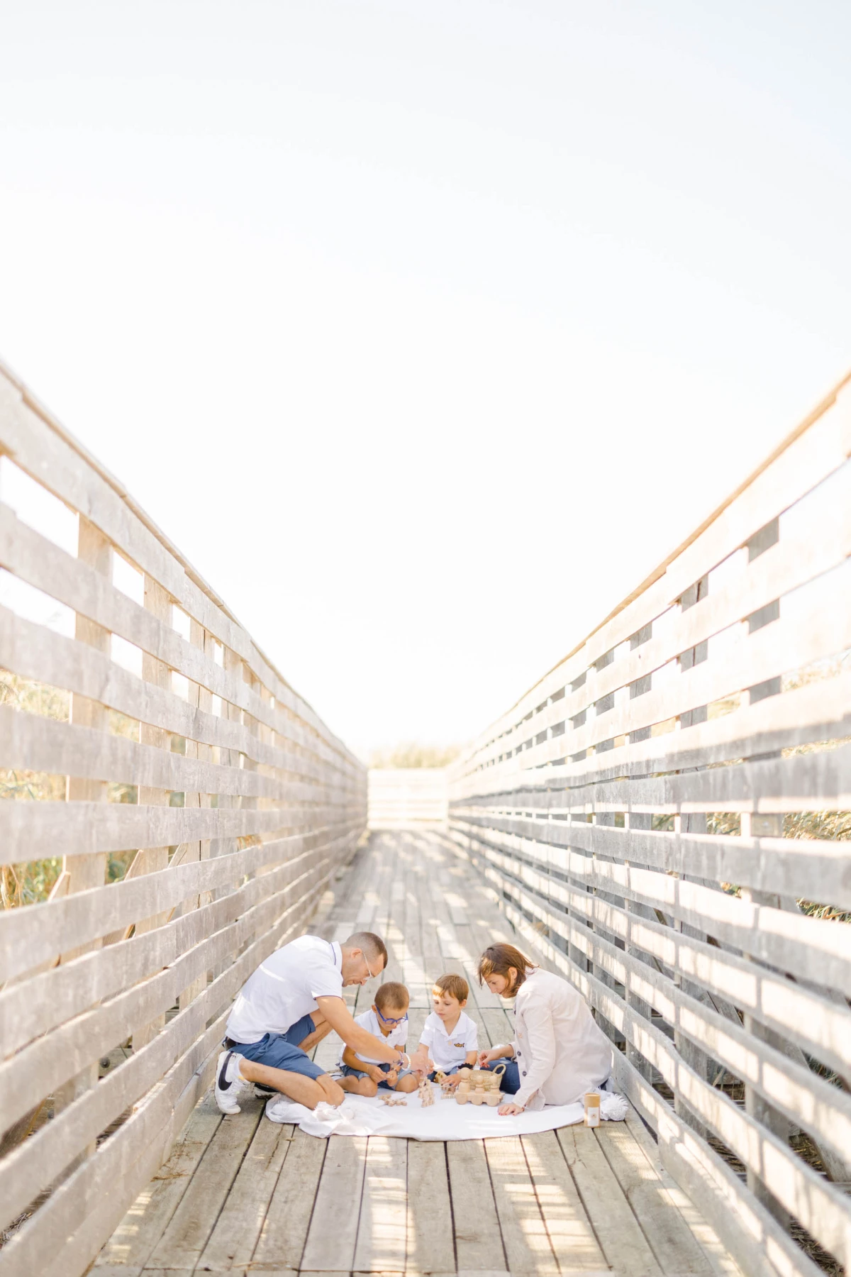 Mère et ses trois enfants enlacés sur une couverture blanche, entre deux murs lumineux en bois