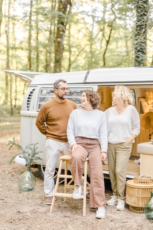 Trois générations de femmes souriantes assisses devant un camping-car vintage en forêt, moment de complicité familiale dans une ambiance chaleureuse et intemporelle