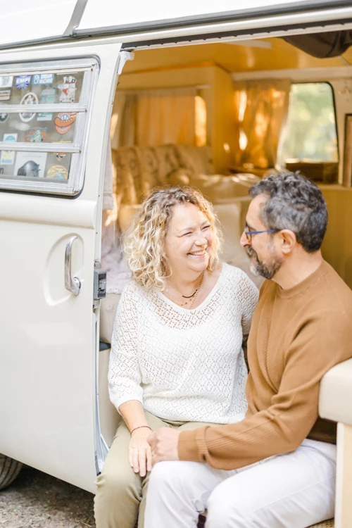 Couple complice assis dans un van aménagé, souriant avec tendresse, lumière dorée, ambiance intime et authentique