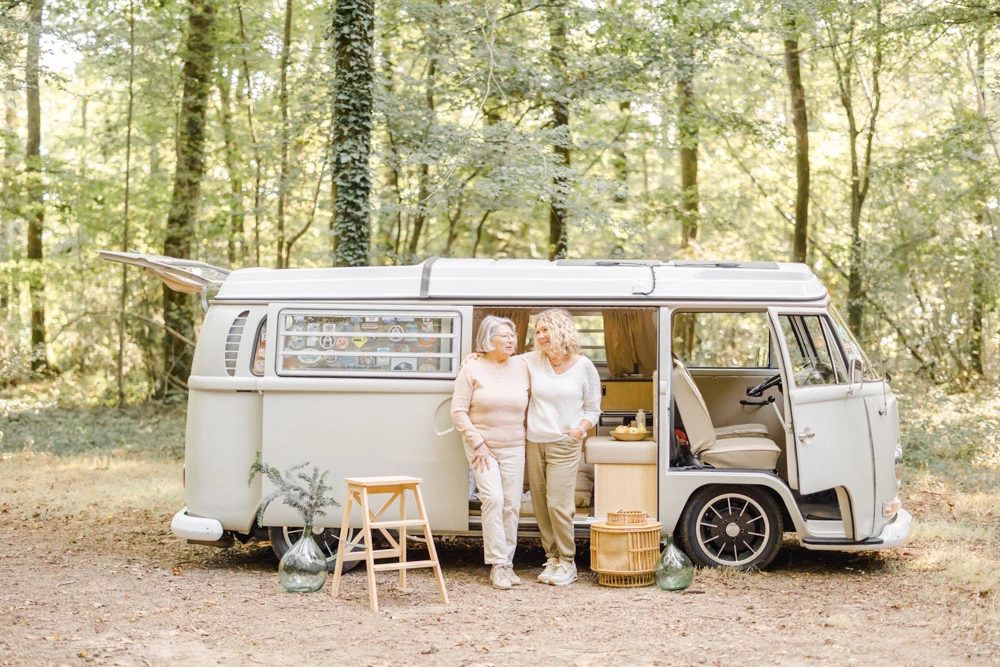 Séance famille portrait devant un camping-car blanc en forêt, deux personnes assises dans une ambiance chaleureuse et intime en pleine nature