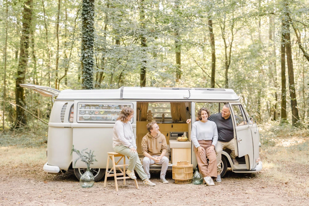 Séance famille vintage dans une caravane rétro en forêt, quatre personnes partageant un moment de complicité et tendresse sous une lumière dorée naturelle