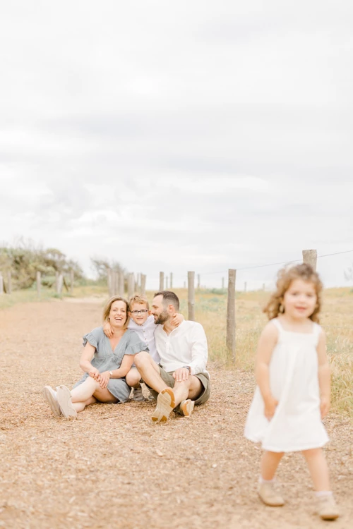 Famille heureuse assise dans un chemin de campagne avec leur fille en robe blanche marchant devant