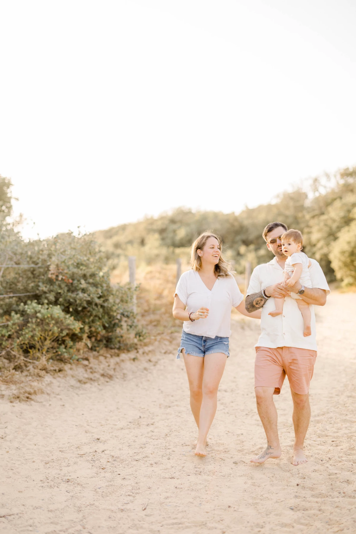 Famille marchant pieds nus sur un chemin ensoleillé, parents tenant leur enfant dans une ambiance lumineuse