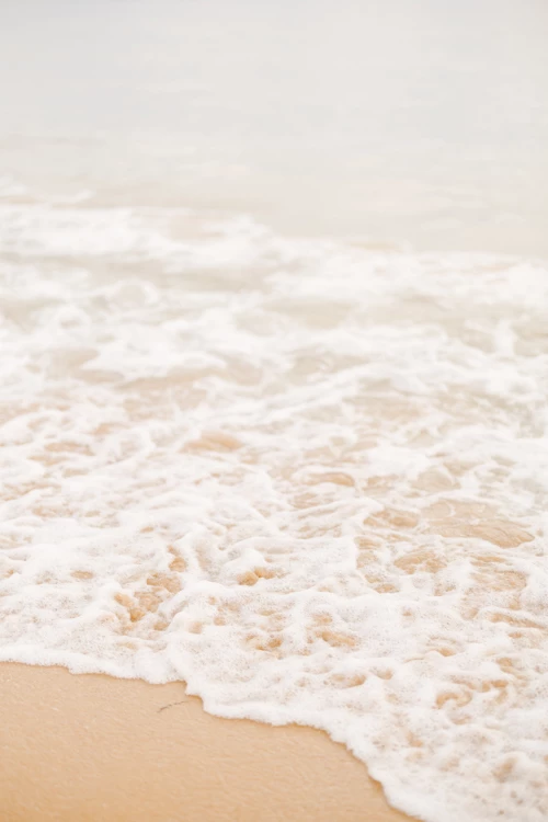 Vague délicate venant lécher le sable doré d'une plage, créant une écume blanche et une atmosphère apaisante