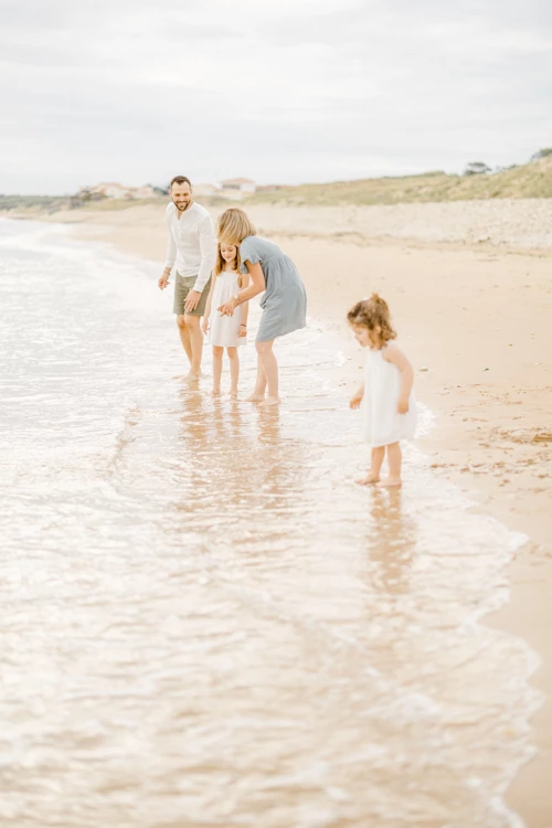 Famille en tenue claire jouant pieds dans l'eau sur une plage de sable fin lors d'une belle journée d'été
