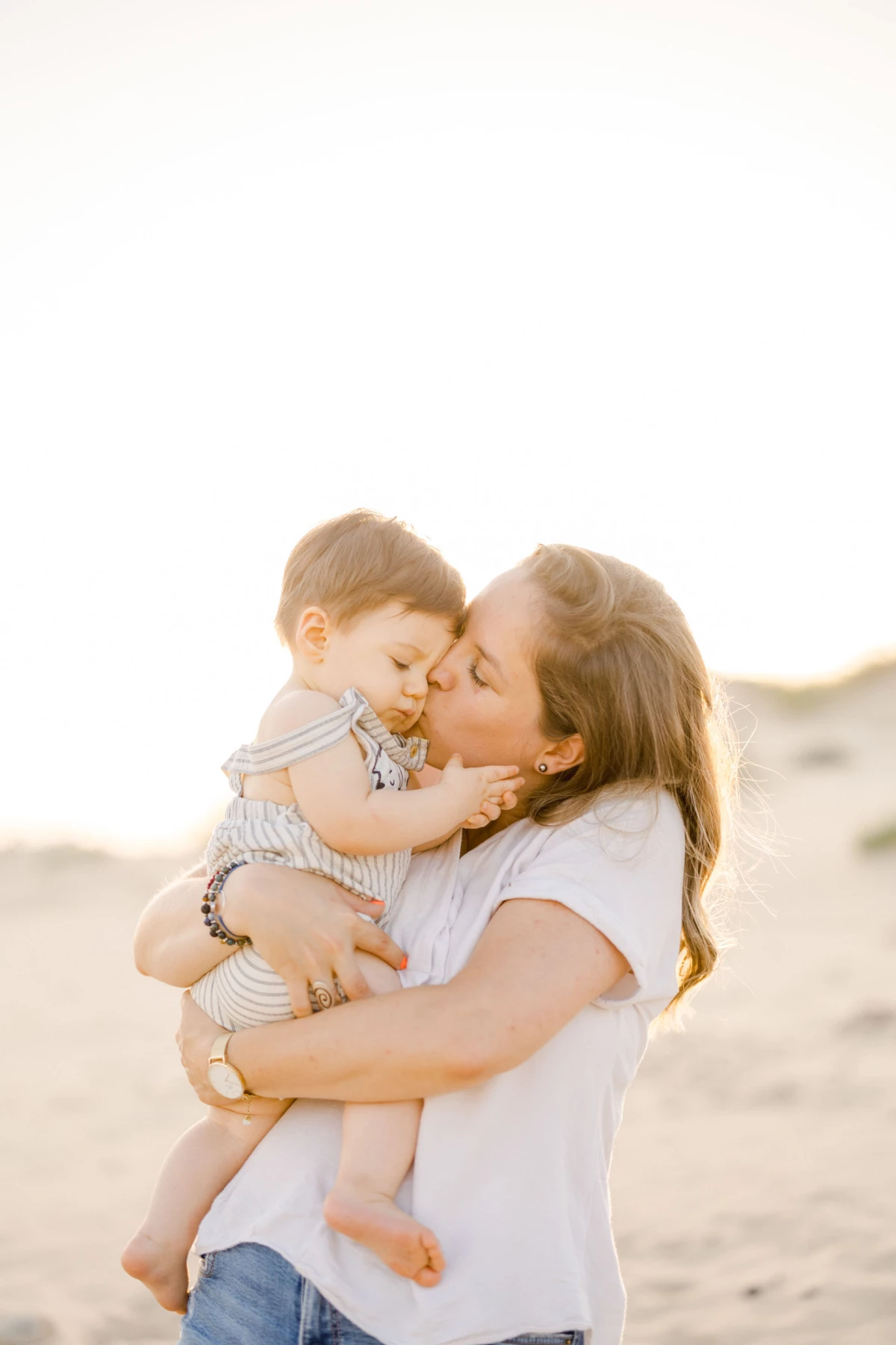 Mère embrassant tendrement son jeune enfant sur une plage au coucher du soleil
