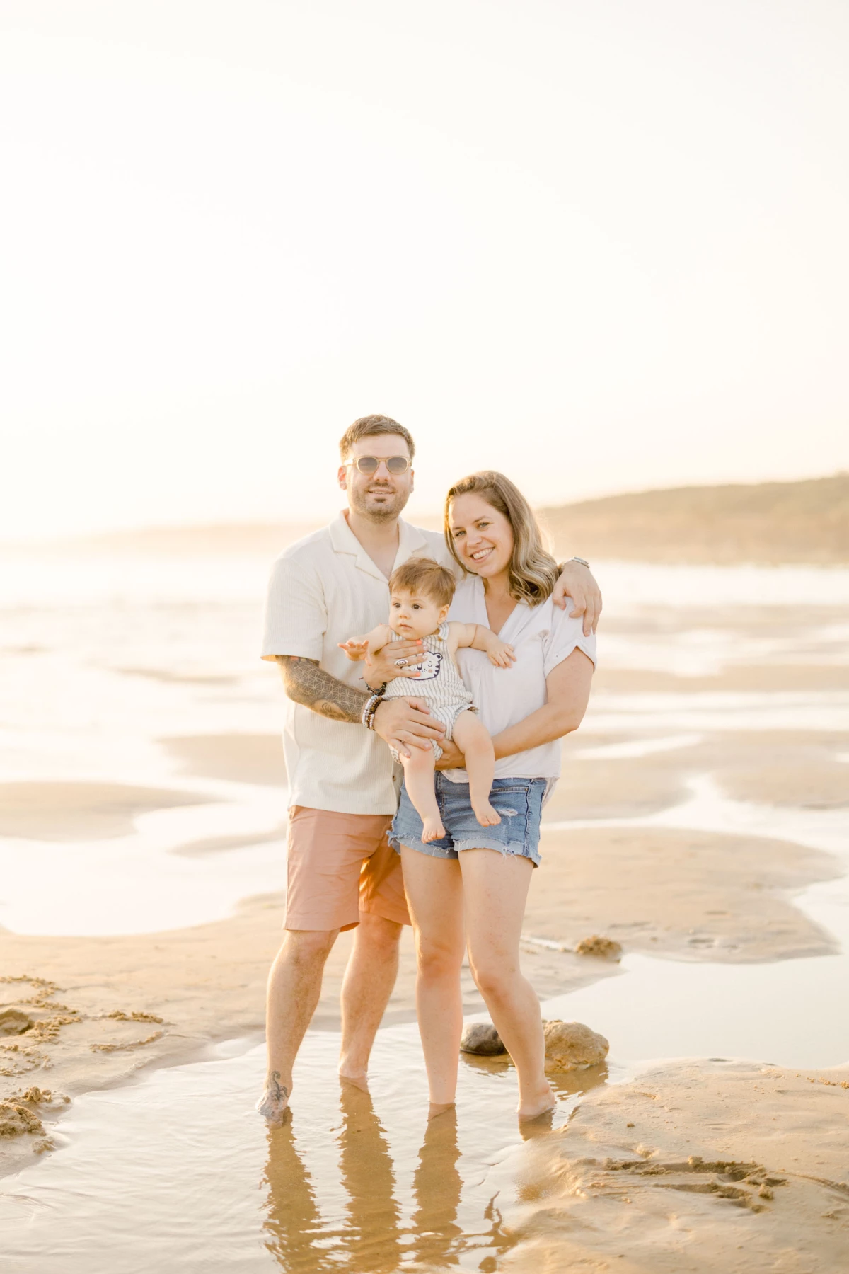 Famille de quatre personnes sur une plage au coucher de soleil, parents tenant leurs deux jeunes enfants