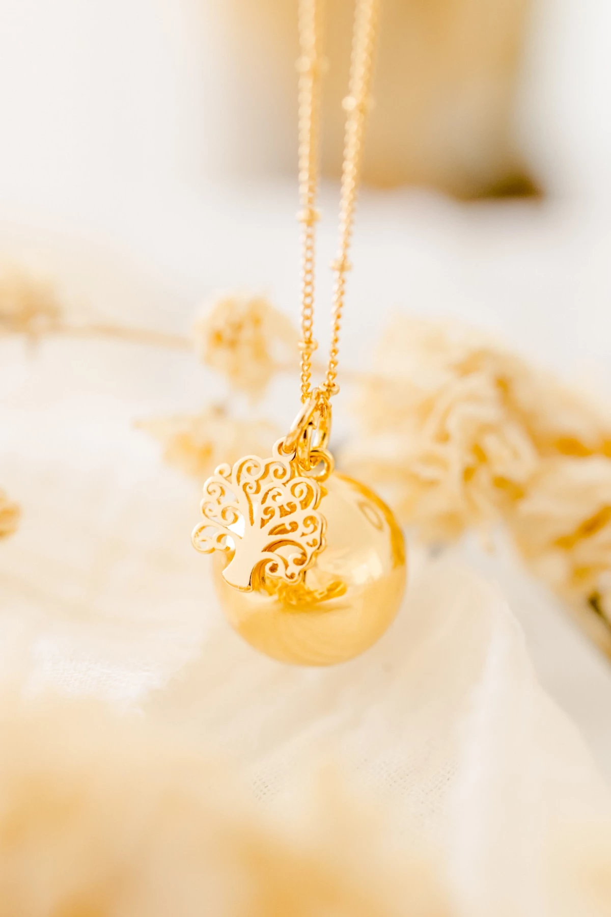 Collier de mariée doré avec pendentif arbre de vie sur perle nacrée, posé délicatement sur dentelle blanche