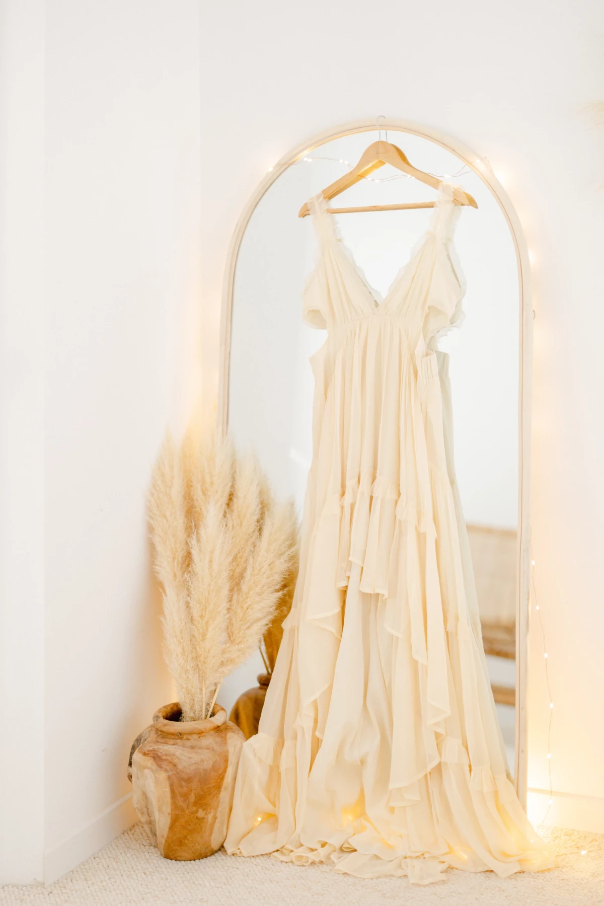 Robe de mariée ivoire suspendue devant miroir arche avec herbe de pampa séchée en décoration