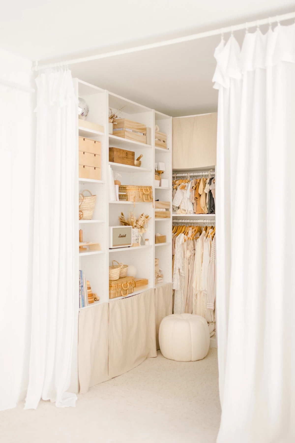 Dressing élégant aux tons blanc et beige avec étagères organisées et vêtements suspendus derrière rideaux blancs