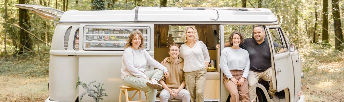 Séance famille multigénérationnelle dans un van vintage, six personnes souriantes posant avec complicité et tendresse, lumière naturelle dorée, ambiance chaleureuse et intemporelle en forêt