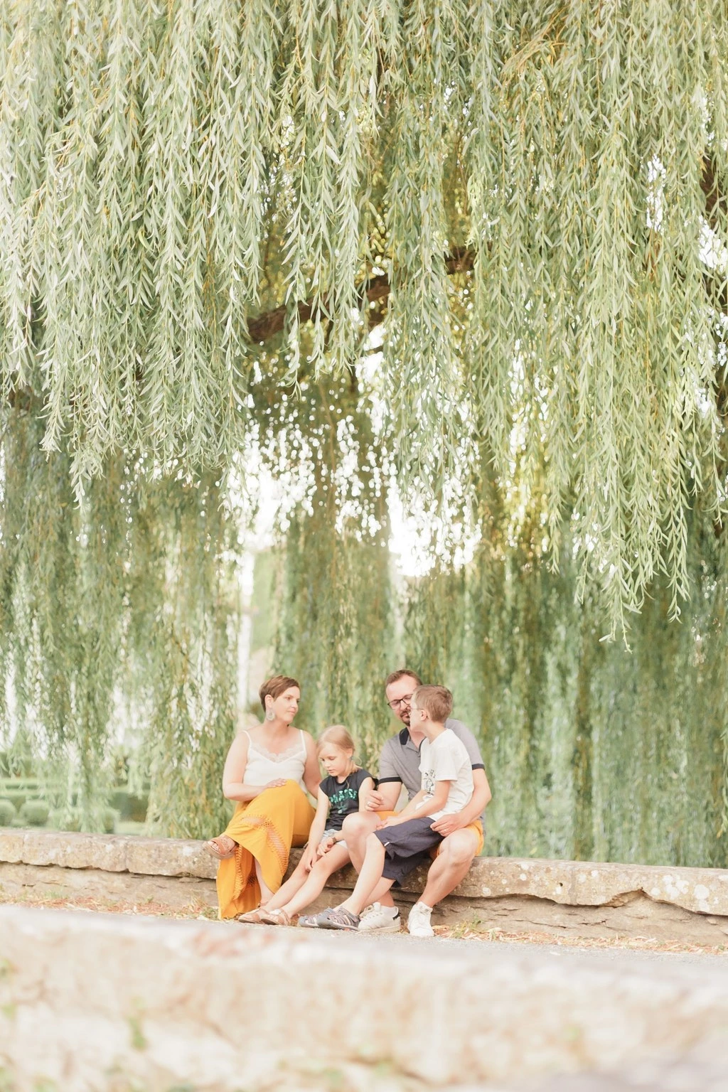 Séance photo famille en bord de fleuve sous un saule pleureur, trois enfants et une mère dans une ambiance tendre et lumineuse, moments d'authenticité et complicité en Vendée