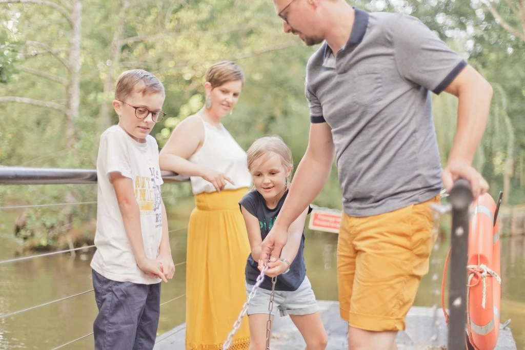 Séance famille en extérieur : père et enfants pêchent ensemble au bord de l'eau, moment de complicité et tendresse dans une ambiance lumineuse et chaleureuse