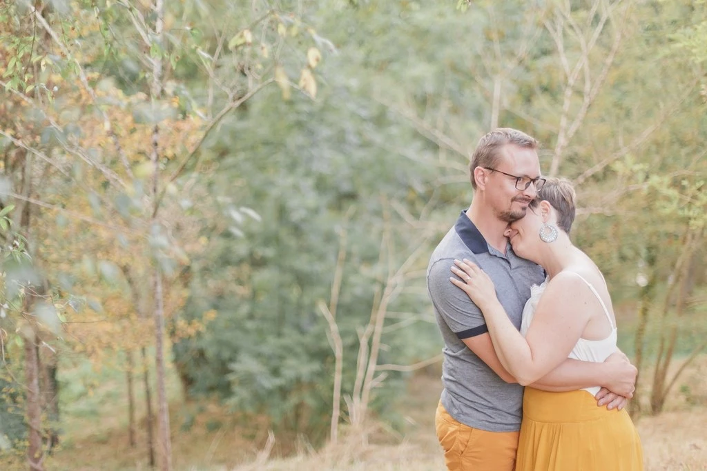 Séance couple en extérieur : homme et femme s'enlacent tendrement dans une forêt dorée, lumière naturelle douce, ambiance romantique et intemporelle