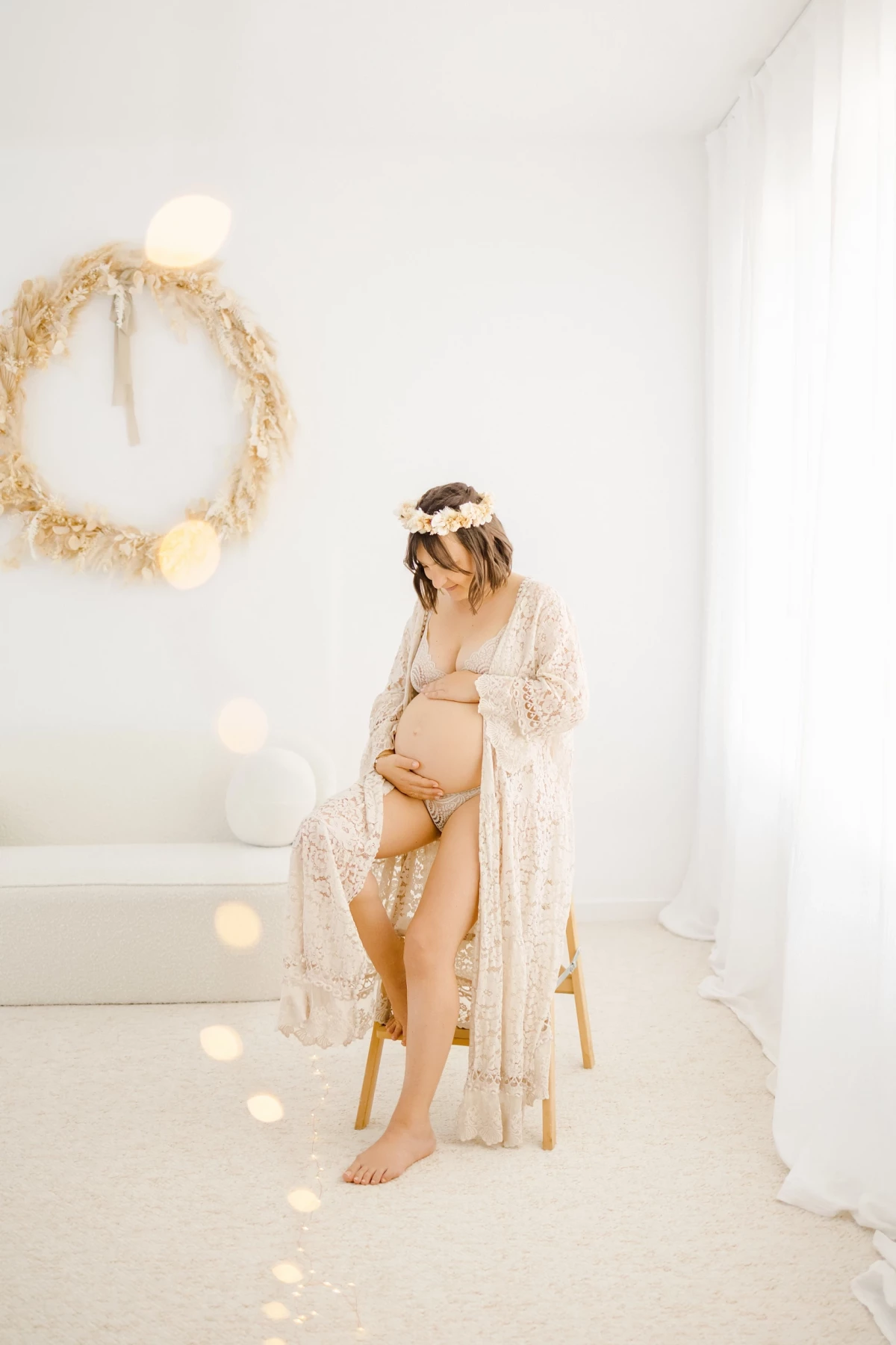 Séance grossesse en studio : future maman caresse son ventre rond dans une robe blanche dentelle, ambiance lumineuse et intimiste