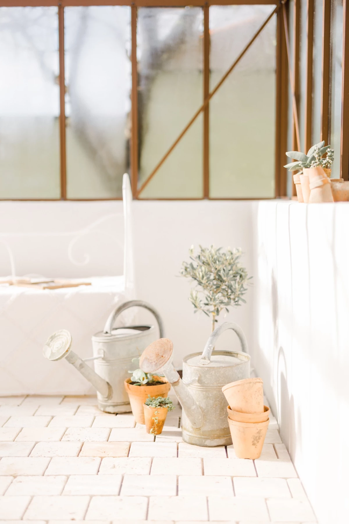 Décoration studio de photographie : arrosoirs blancs et pots de fleurs disposés sur un sol en bois clair sous une verrière lumineuse