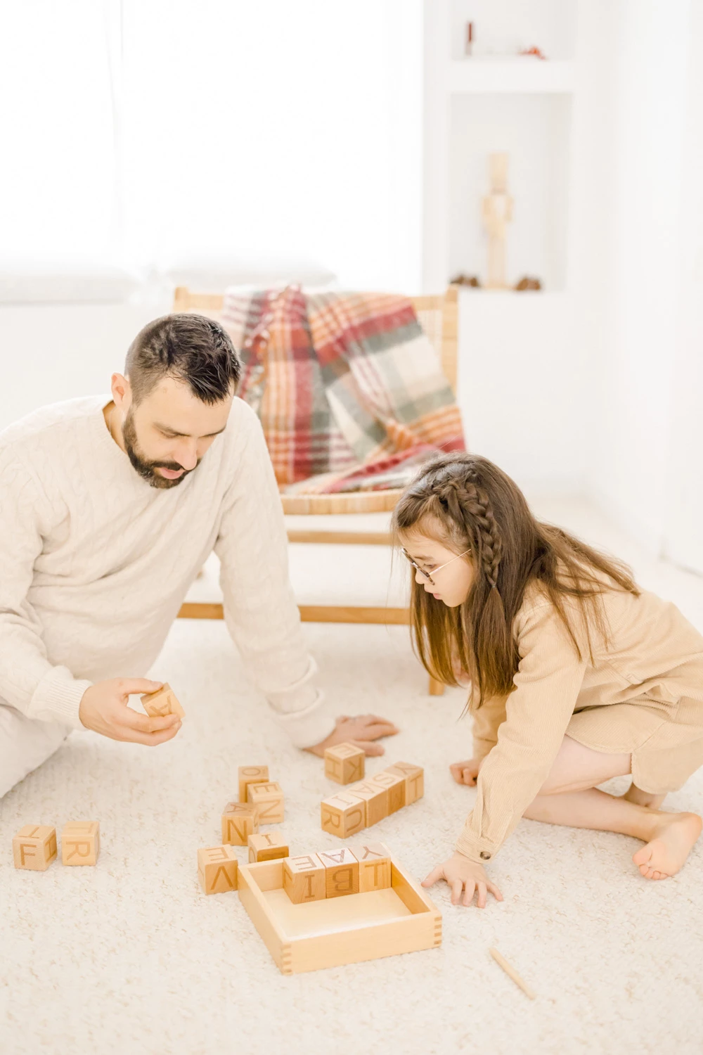 Séance famille intime : père et fille jouent avec des blocs de bois sur un tapis blanc, complicité tendre dans une lumière douce et chaleureuse