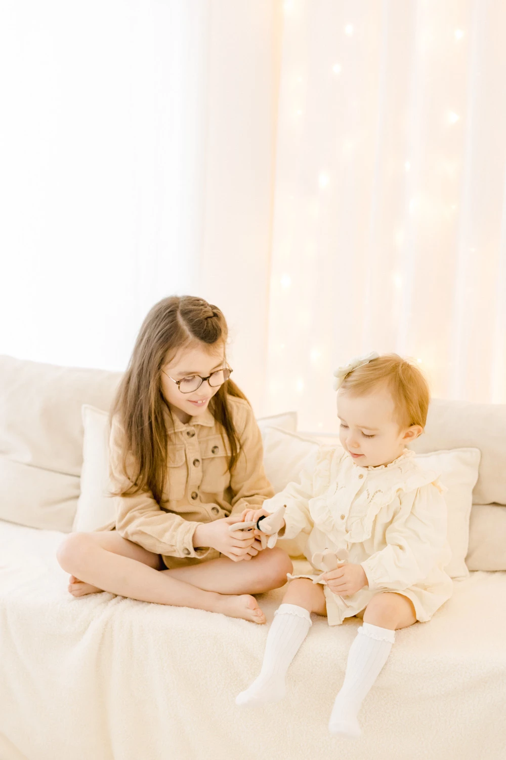 Séance photo famille : deux enfants assis sur un lit blanc partagent un moment de complicité et tendresse dans une lumière dorée et douce