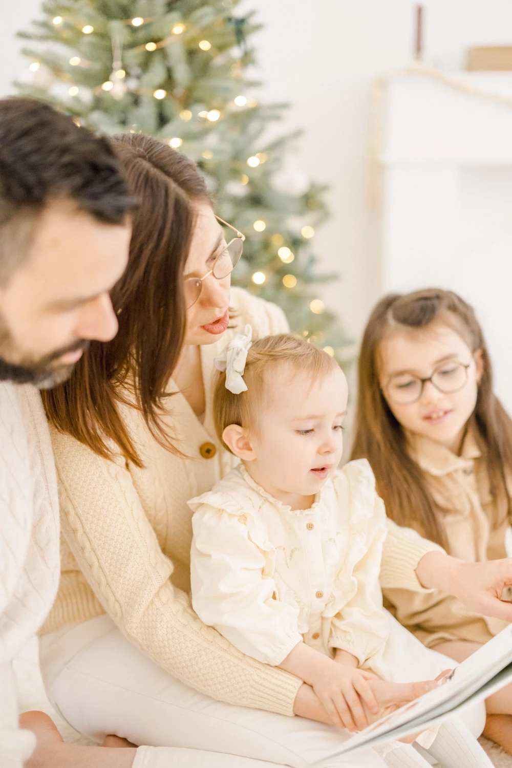 Séance photo famille en studio - mère et deux enfants en tenues crèmes devant sapin de Noël illuminé, moment de complicité et tendresse