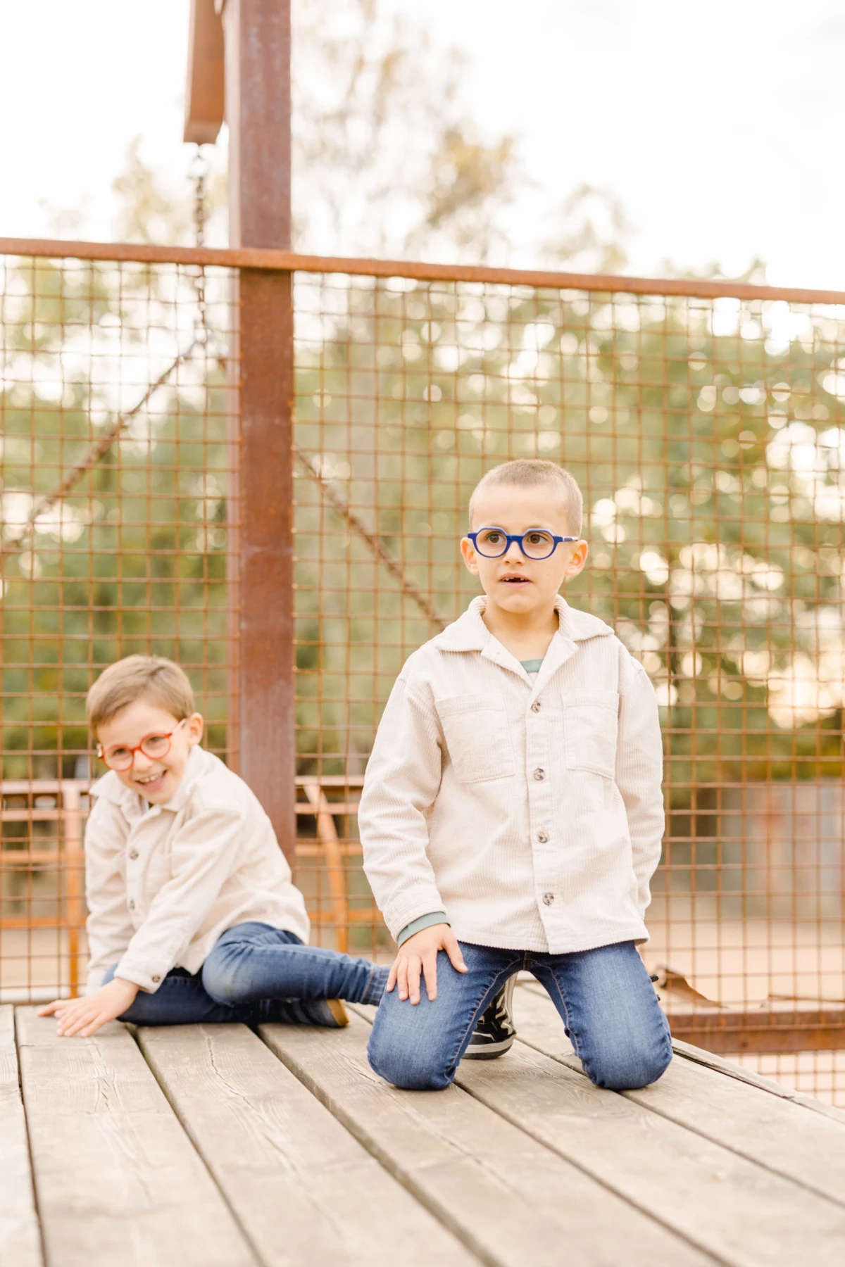 Deux jeunes frères à lunettes posant en extérieur sur une terrasse en bois avec une ambiance naturelle